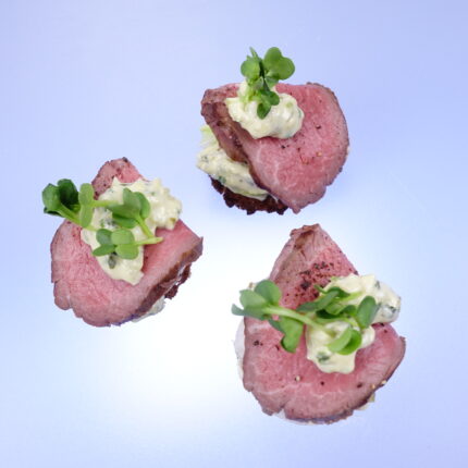 Drei Canapé Häppchen mit Rinderfilet, Remoulade und Kräutern. Hintergrund ist blau.