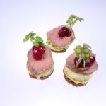 Drei Canape Häppchen, belegt mit rosa Roastbeef und Deko.